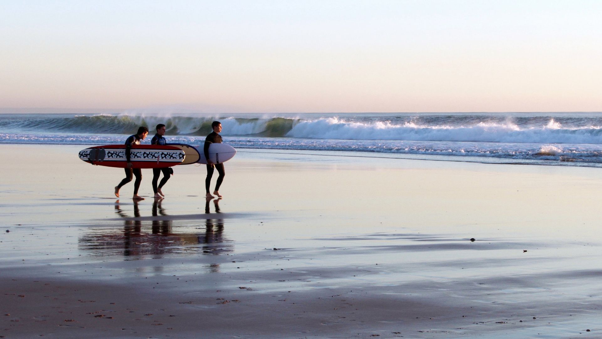 Three surfers are walking on the beach carrying their surfboards. Carcavelos, Lisbon.