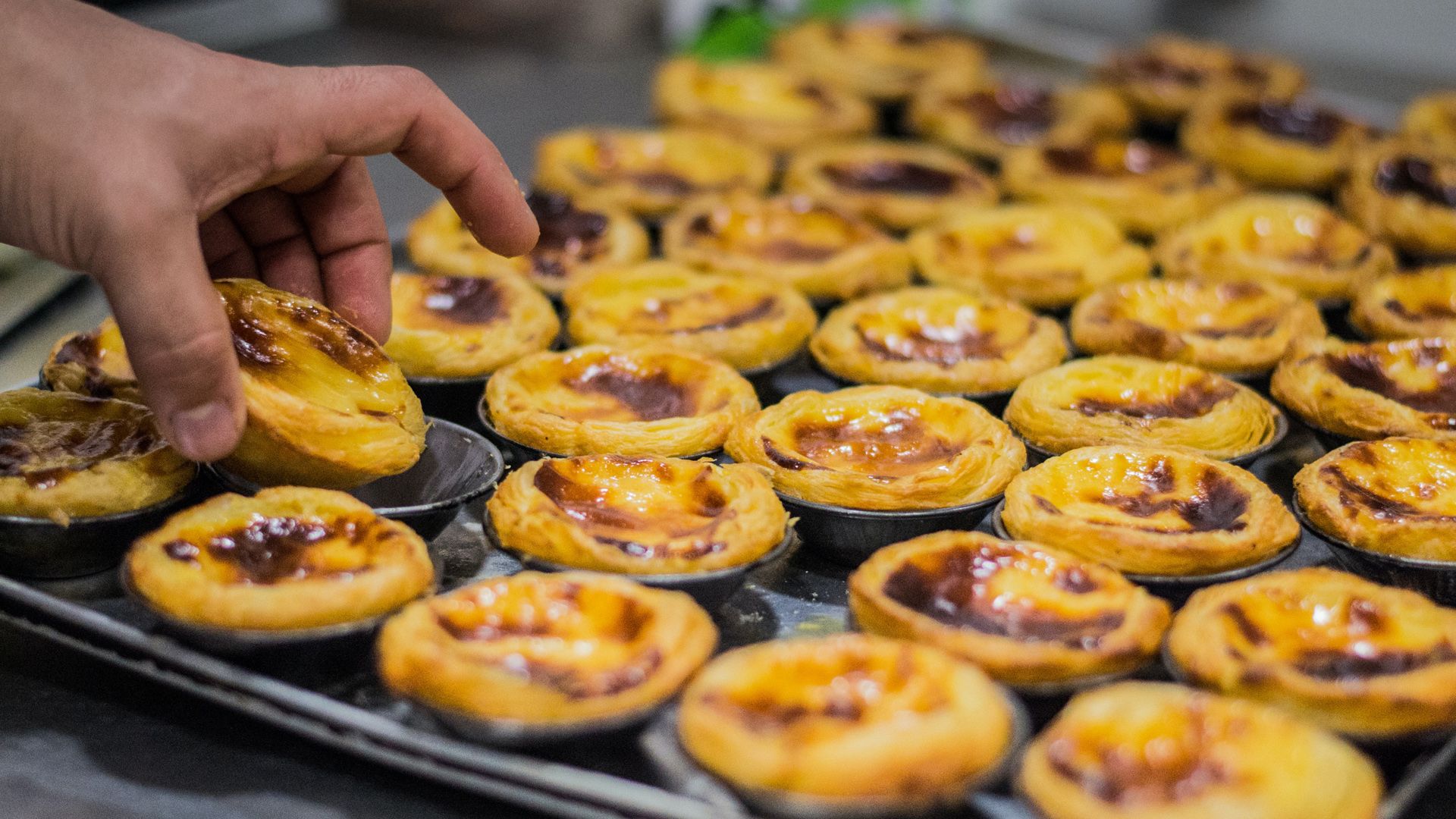 A person is picking up a pastry from a tray of pastries. Pastel