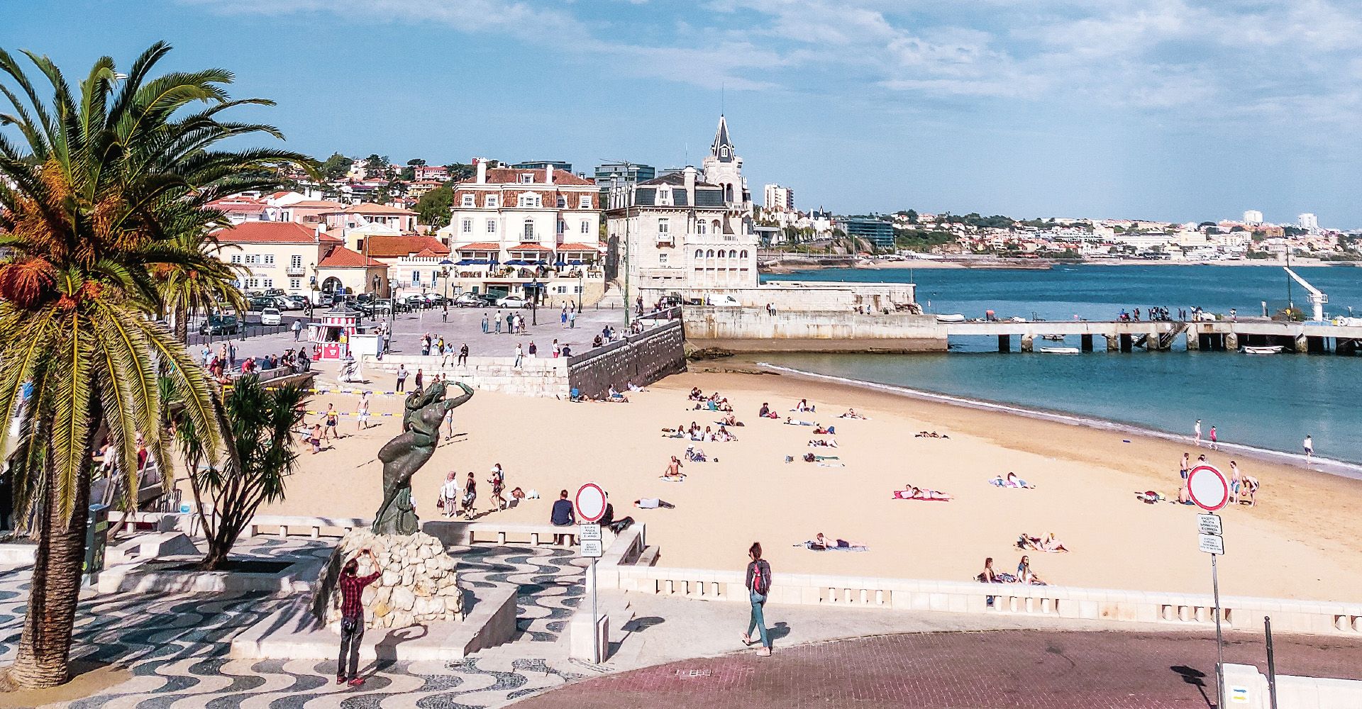 A beach in Cascais with palm trees and a city in the background