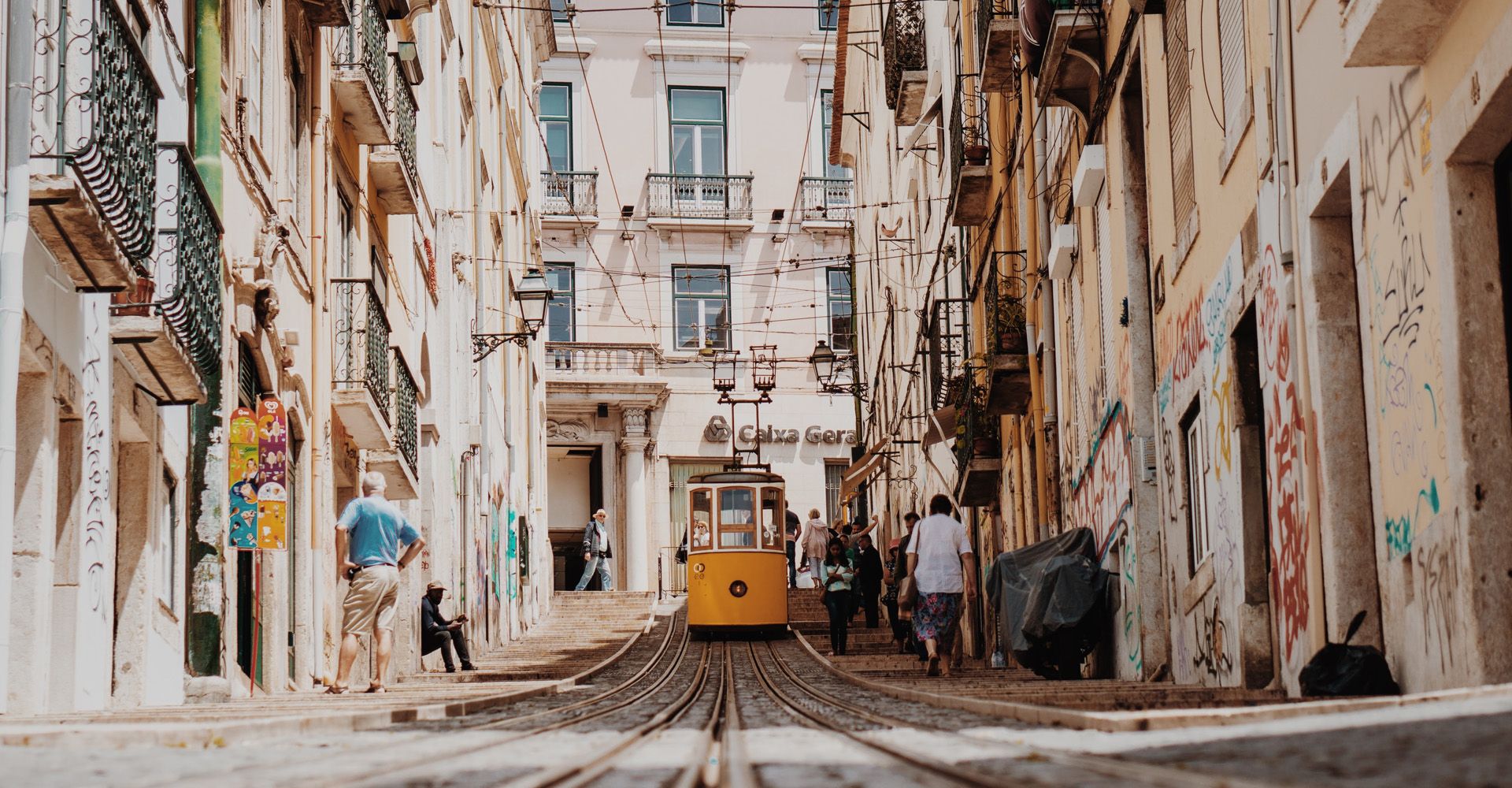 A yellow Lisbon Lift is going down a narrow street in a city.