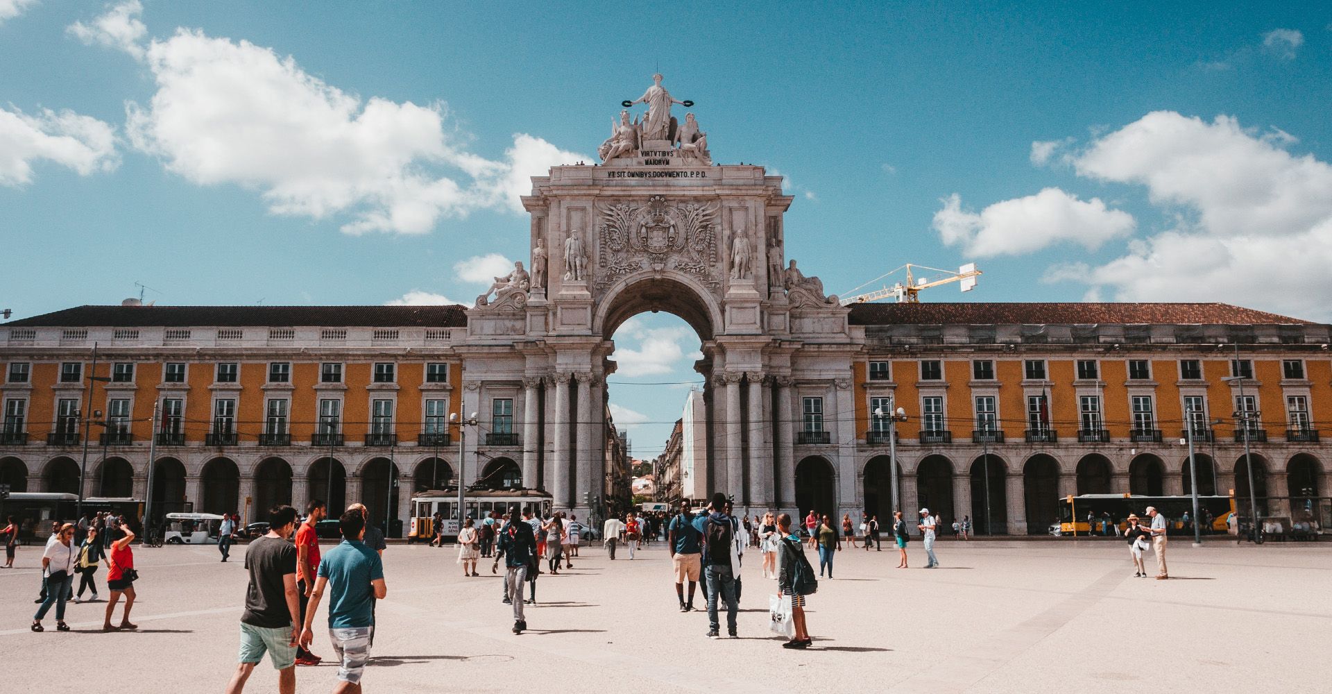 A group of people are walking in front of a large building in Praça do Comércio, Lisbon.