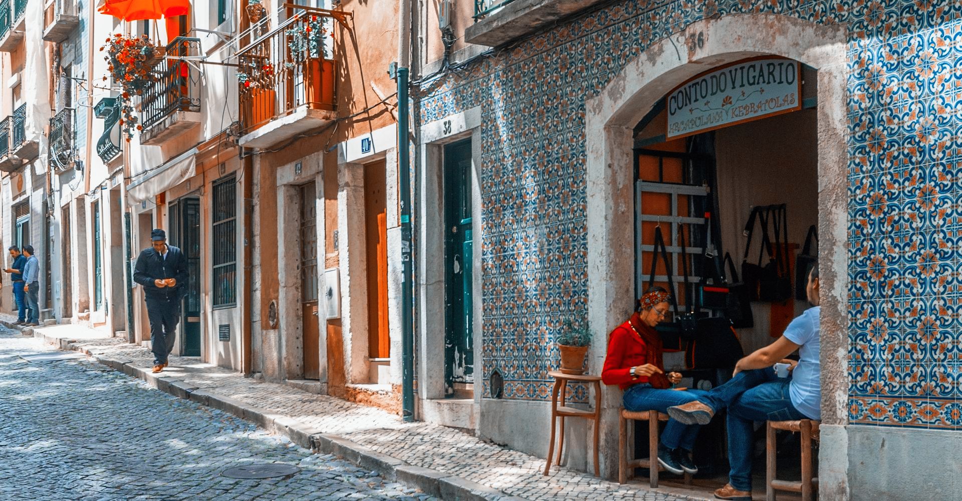 A couple of people are sitting outside of a store on a cobblestone street in Alfama, Lisbon