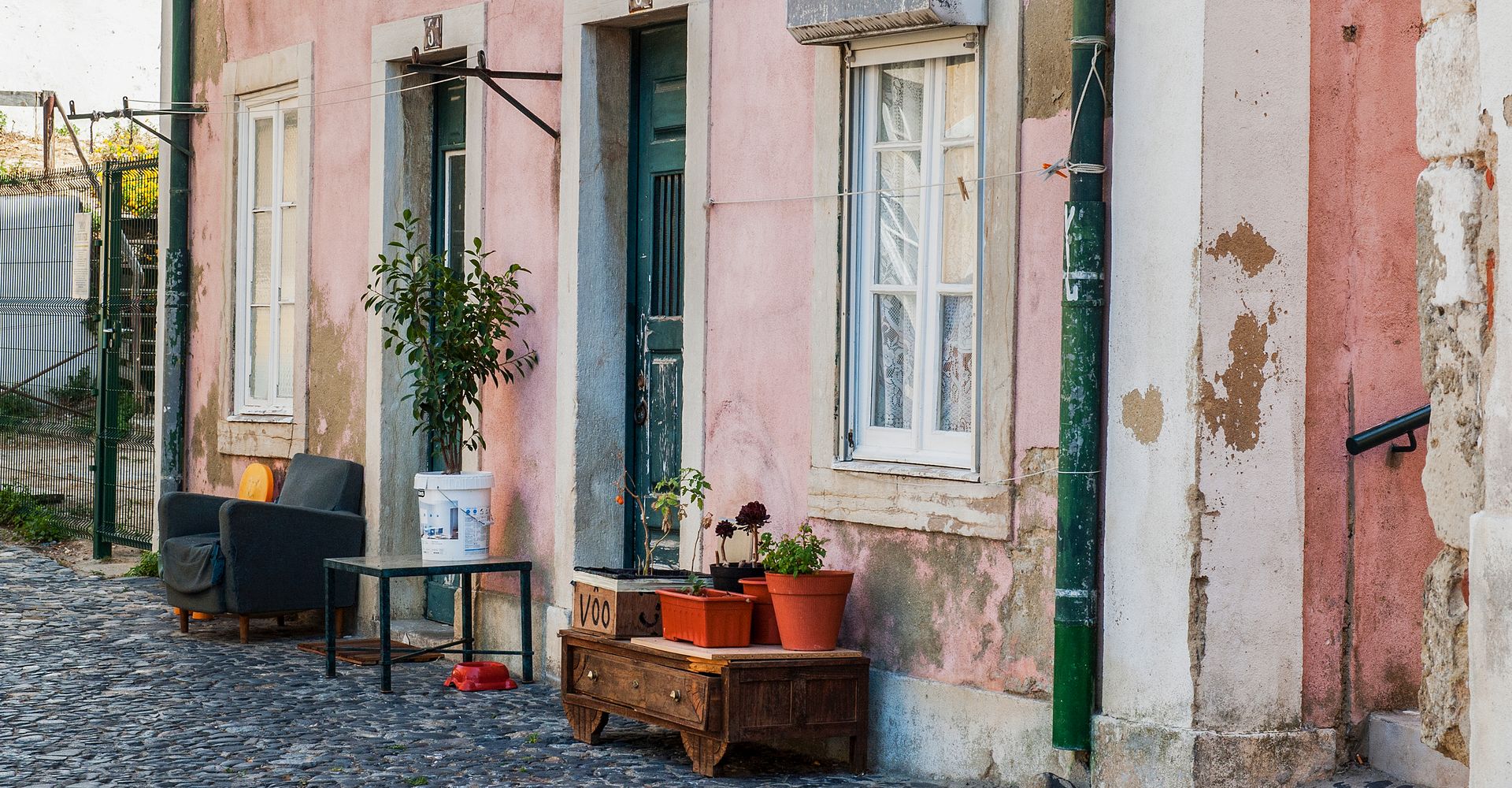 A pink building with potted plants in front of it on a cobblestone street in Alfama, Lisbon.